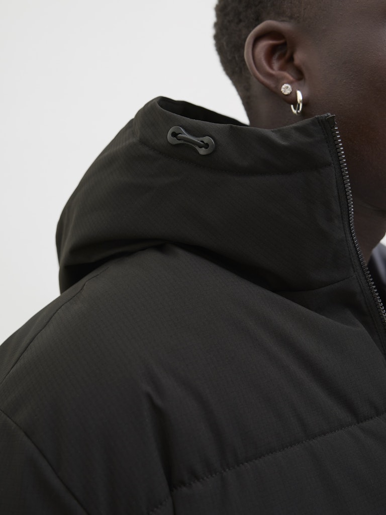 Person wearing a black jacket with a hood on a light gray background