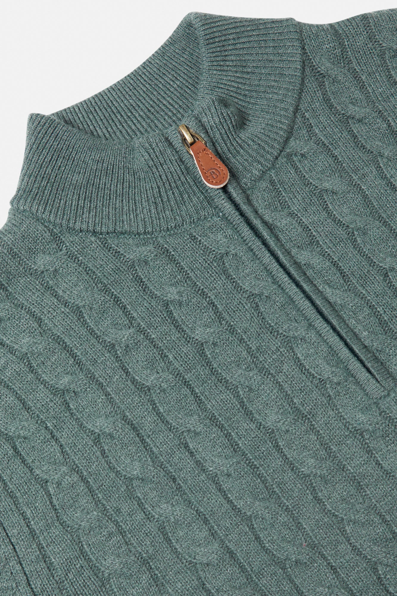 Close-up of a teal cable knit sweater with a leather tag.