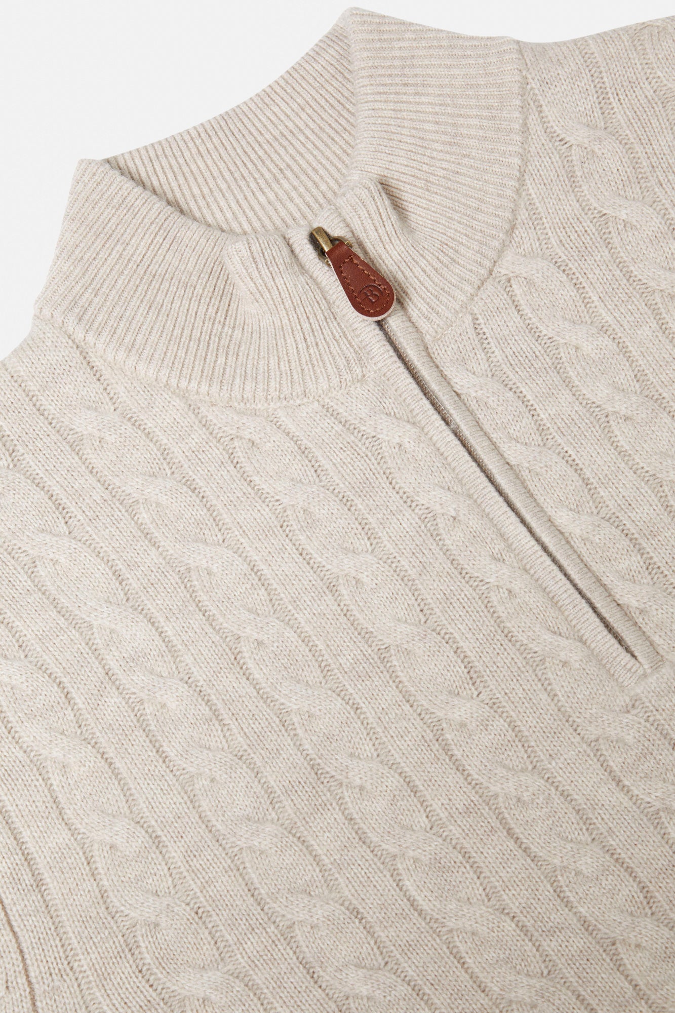 Close-up of a beige cable knit sweater with a zipper and brown button.