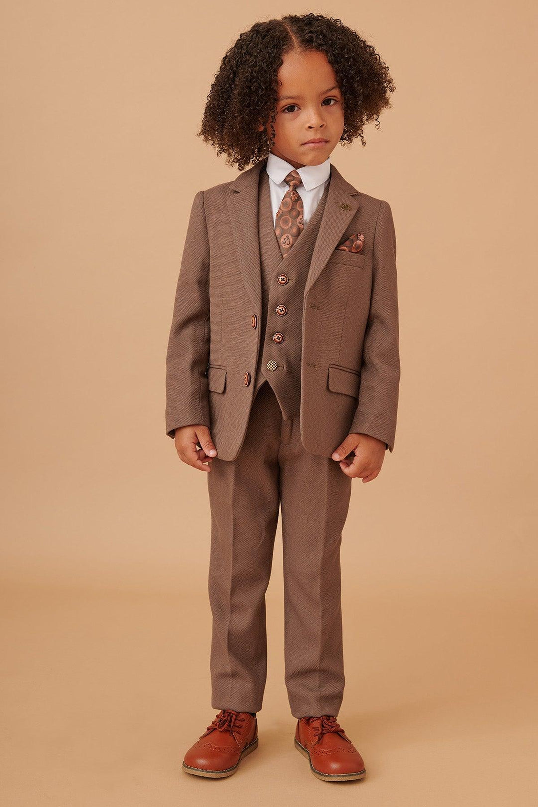 Child wearing a brown suit with a patterned tie against a beige background