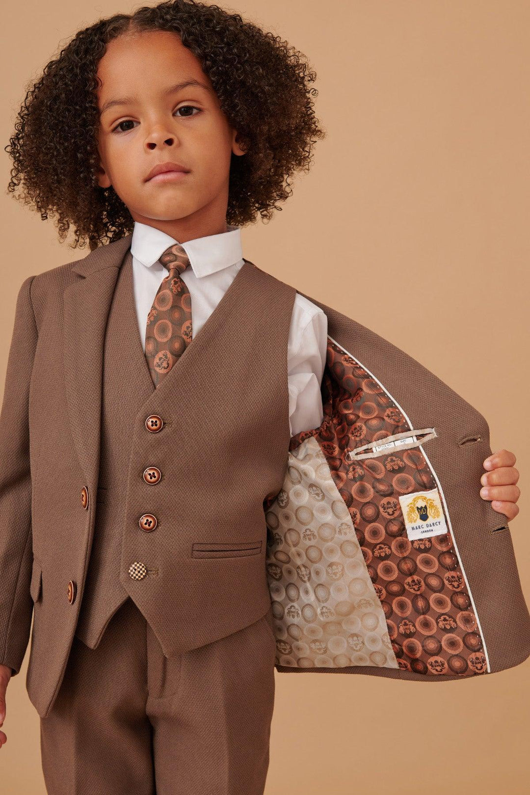 Child wearing a brown suit with a patterned tie against a beige background