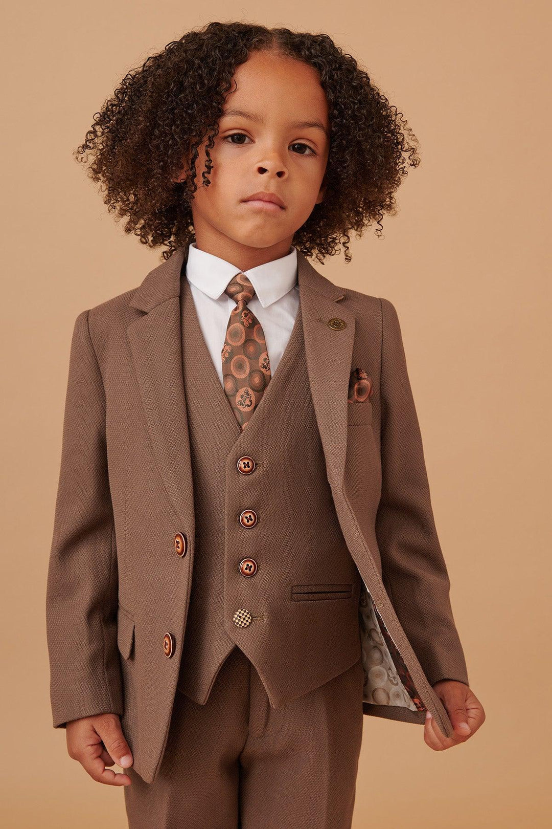 Child wearing a brown suit with a patterned tie on a beige background