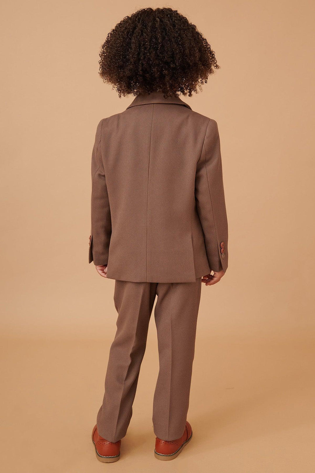 Person wearing a brown suit standing against a beige background