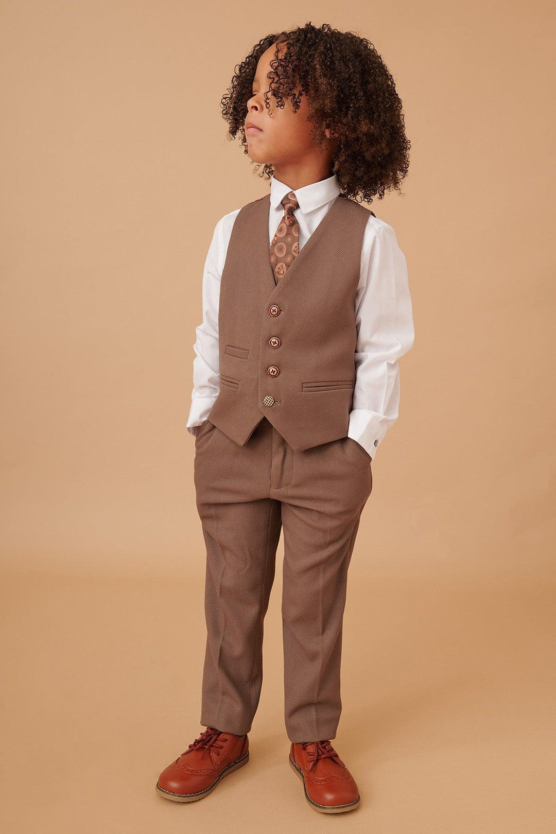 Child wearing a brown suit with a white shirt and red shoes on a beige background