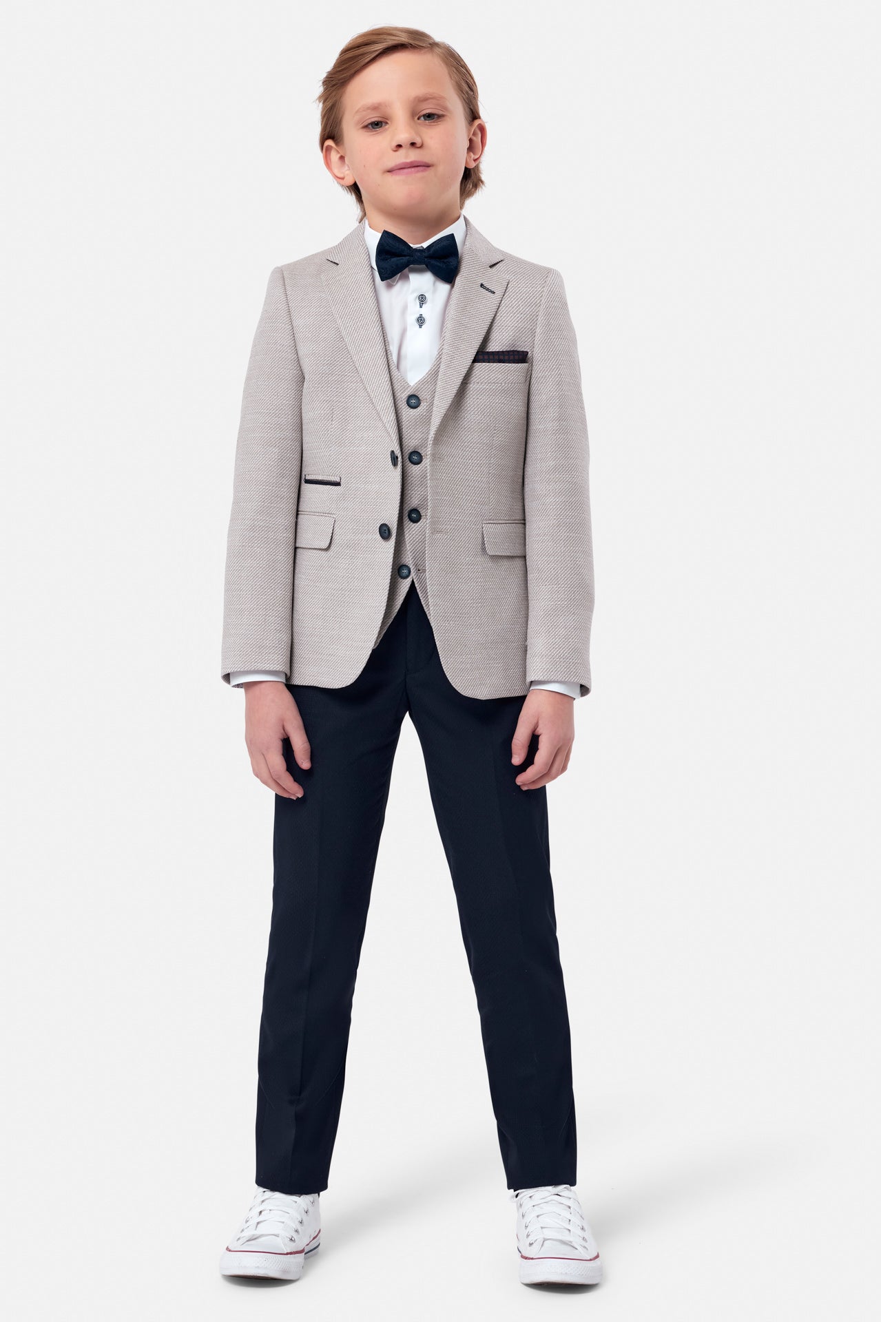 Boy wearing a beige textured blazer with beige waist coat and navy pants full front view