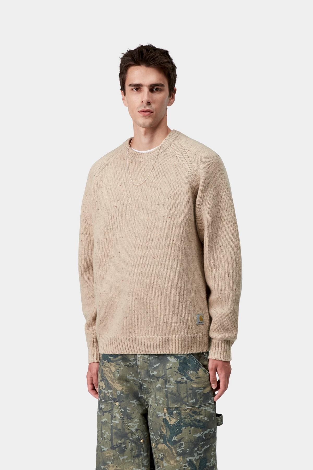 Man wearing a beige sweater and camouflage pants on a white background
