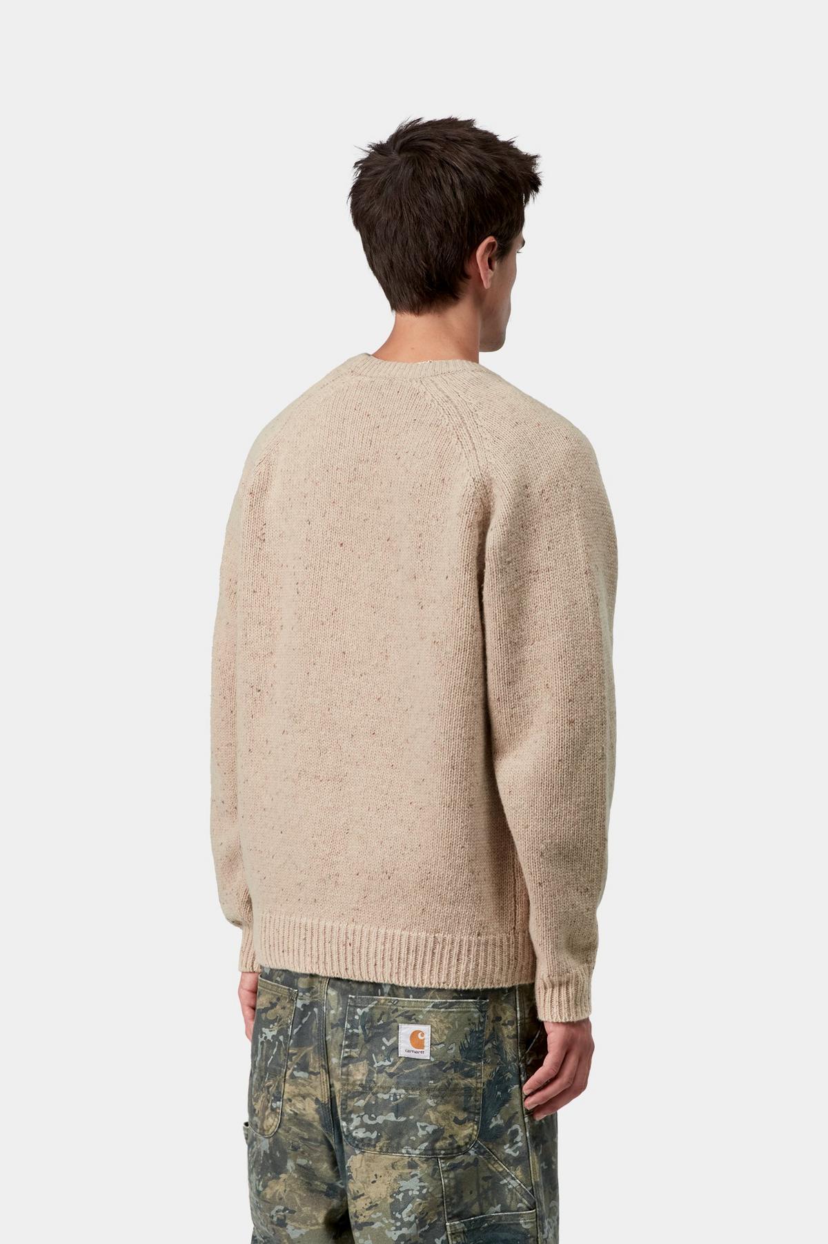 Man wearing a beige sweater and camouflage pants on a white background