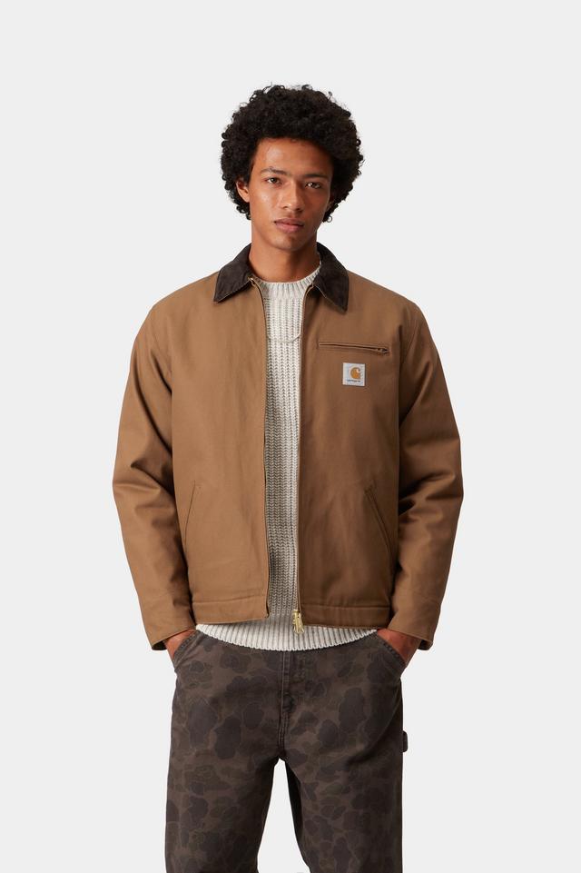 Man wearing a brown jacket with a visible brand logo on a white background