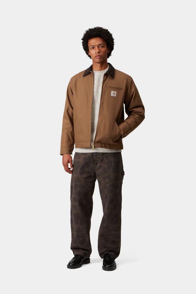 Person wearing a brown jacket and patterned pants on a white background