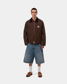 Carhartt WIP Detroit Jacket in Tobacco / Black, shown worn by a model in front view with a black corduroy collar, zip front, and chest pocket.