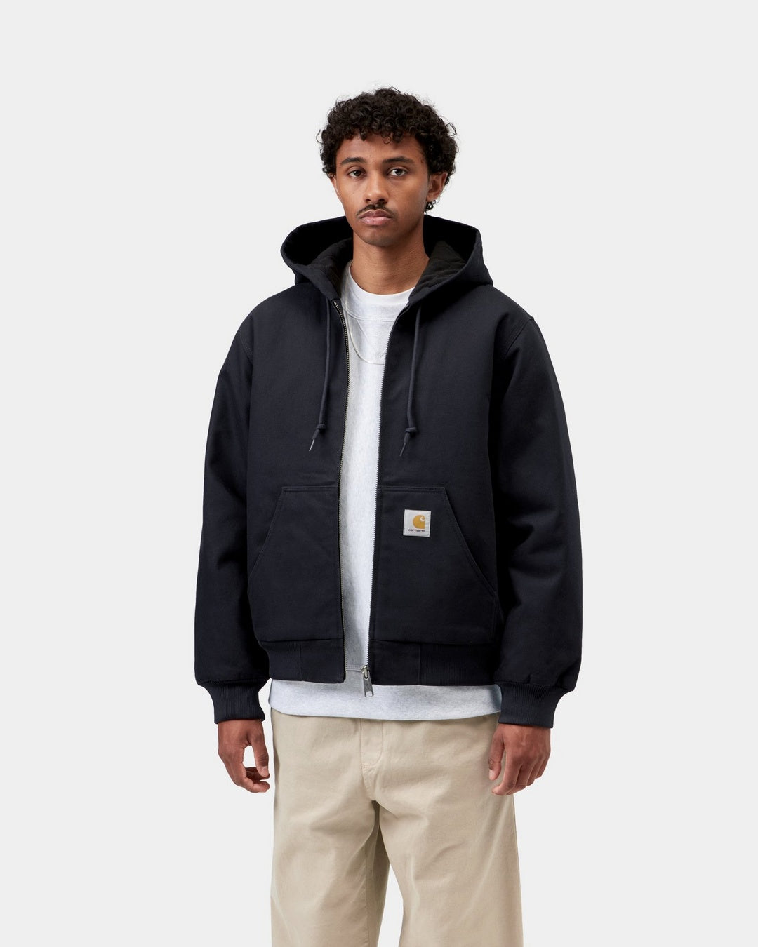 Carhartt WIP Active Jacket in Dark Navy worn by a model, front view. The zip-up hooded jacket has a drawstring hood, ribbed cuffs and hem, a kangaroo pocket, and a square Carhartt logo label on the pocket.