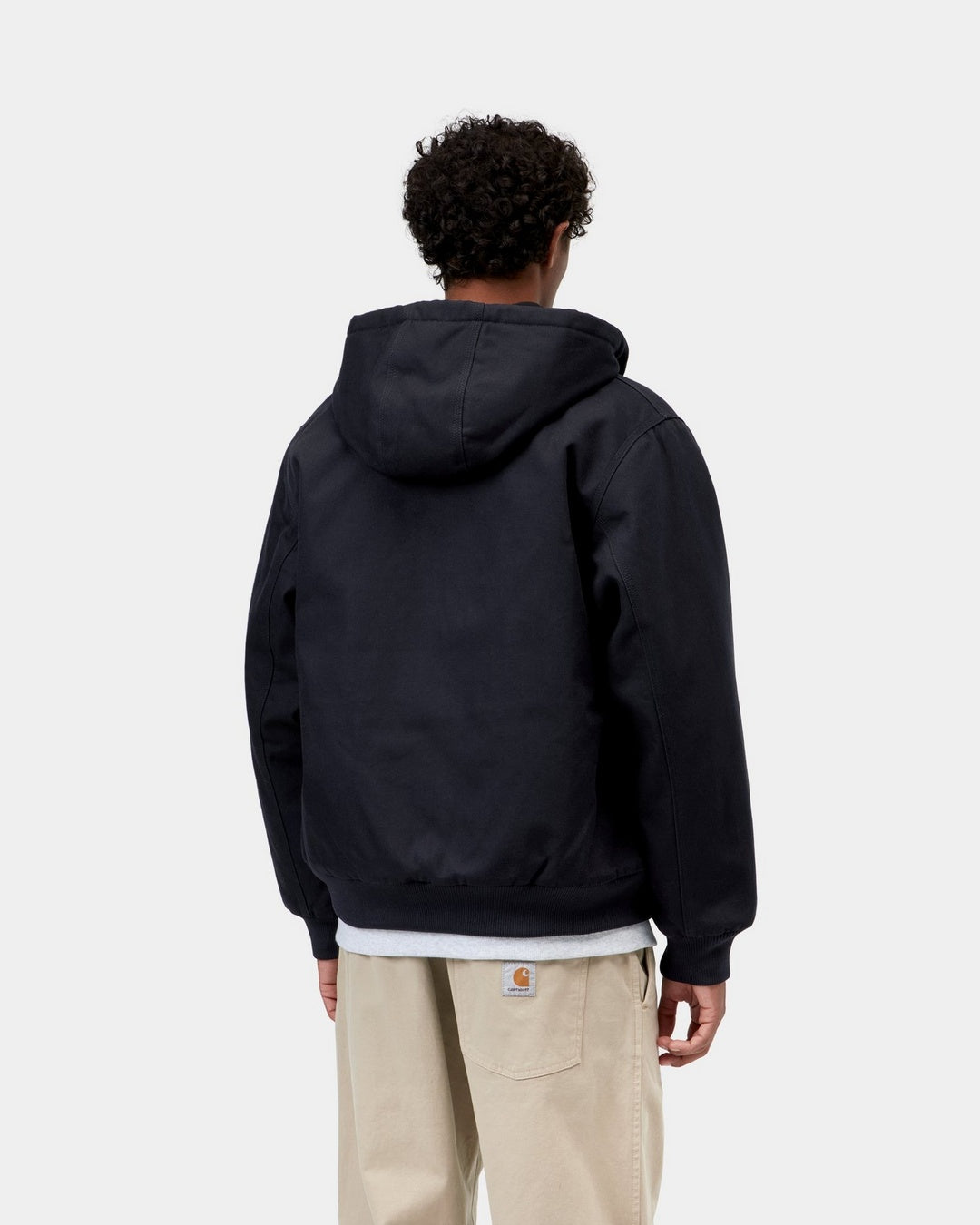 Back view of the Carhartt WIP Active Jacket in Dark Navy worn by a model, showing the hood, ribbed cuffs and hem, and a white layer peeking out beneath.