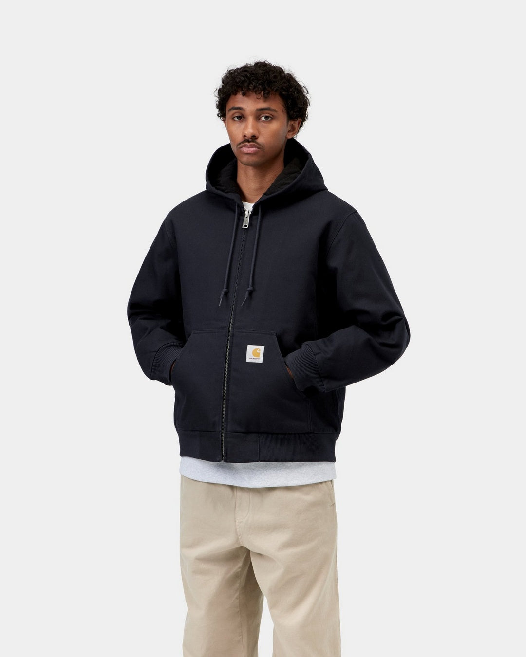 Carhartt WIP Active Jacket in Dark Navy worn by a model, front view with hood up, zipped front, drawstring hood, ribbed cuffs and hem, kangaroo pockets with Carhartt logo patch, hands in pockets.