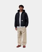 Carhartt WIP Active Jacket in Dark Navy, front view, worn by a model with a white T-shirt and beige trousers. The jacket is zipped with the hood down, showing drawstrings, front pockets, ribbed cuffs and hem, and a square Carhartt label on the left pocket.