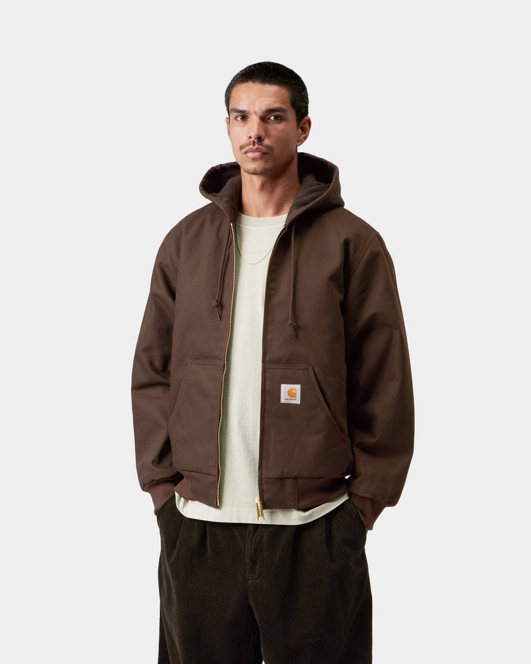 Carhartt WIP Active Jacket in Tobacco worn by a model, front view with hood up, gold-tone zip, kangaroo pockets, and square Carhartt logo patch on the left pocket.