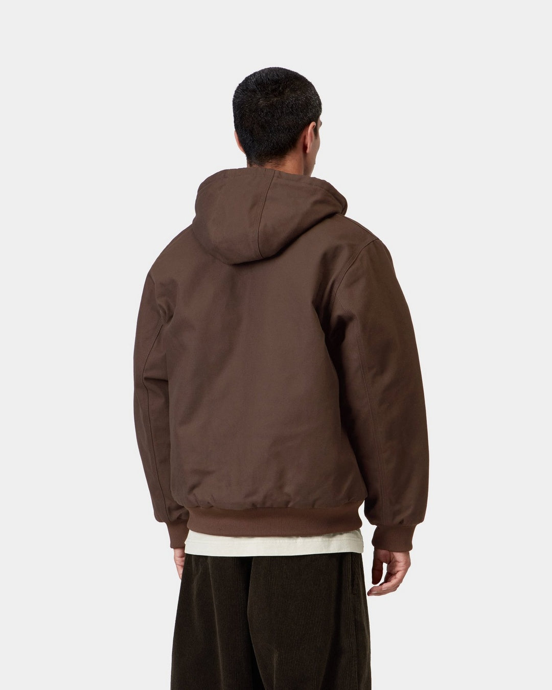 Back view of a model wearing the Carhartt WIP Active Jacket in Tobacco, showing the hood, ribbed cuffs and hem, and the Dearborn Canvas body.