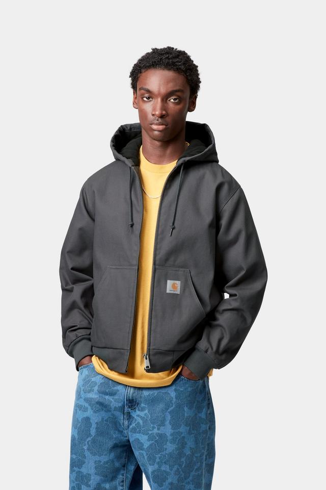 Man wearing a dark gray hoodie jacket over a yellow shirt with blue patterned pants on a white background