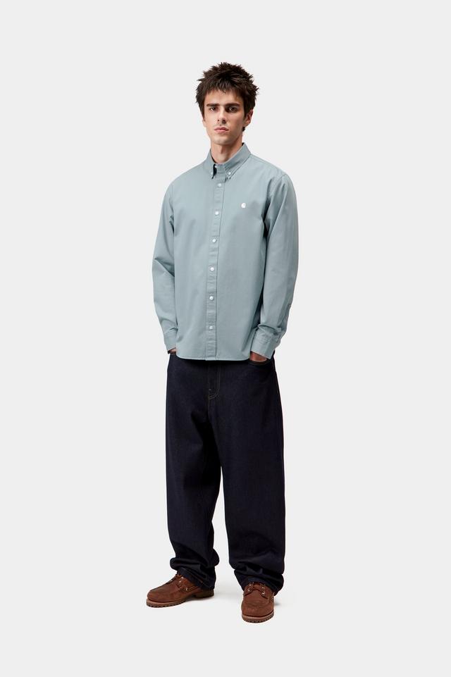 Man wearing a light blue button-up shirt and dark pants on a white background