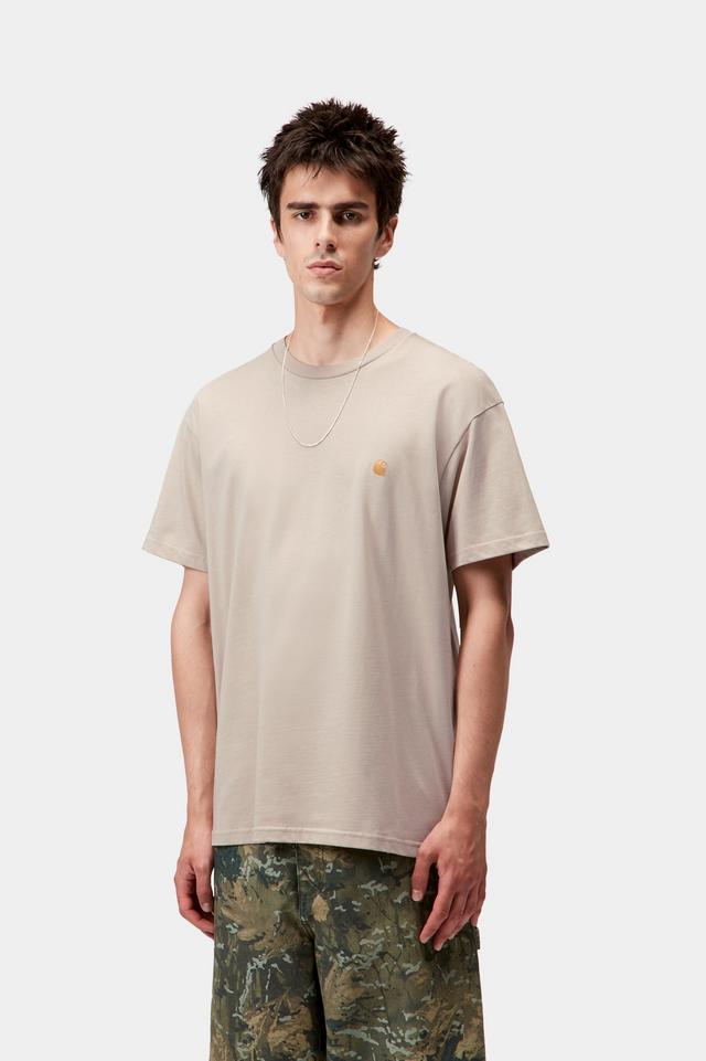 Man wearing a beige t-shirt with a small logo on a white background