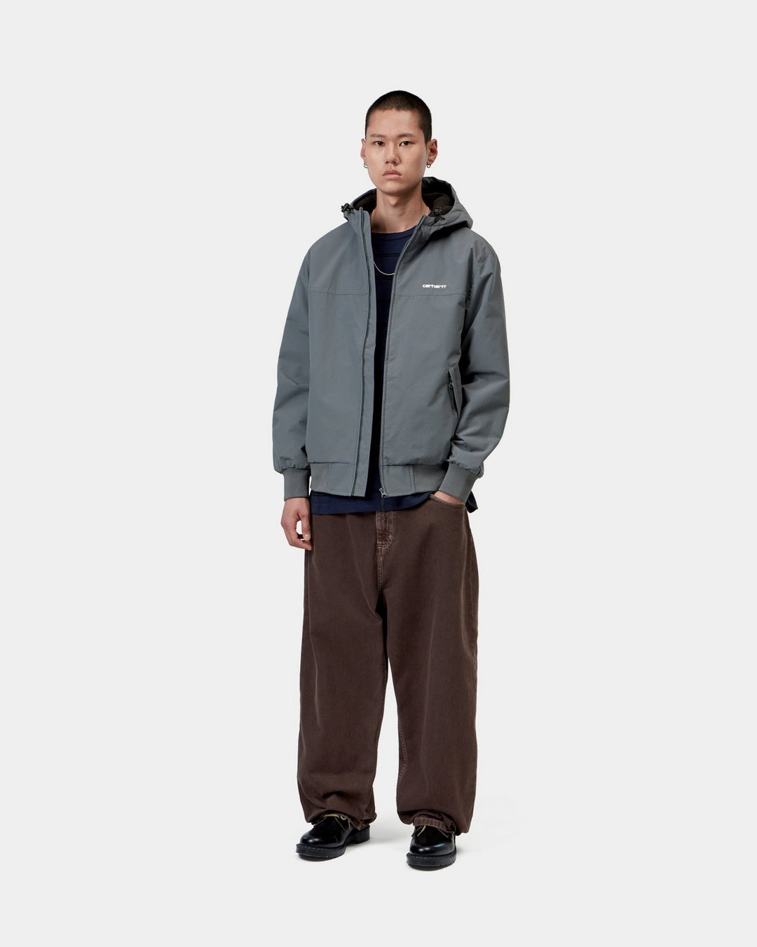Front view of the Carhartt WIP Hooded Sail Jacket in Styx / White worn by a model, showing the zipped hood, chest logo, side pockets, and ribbed cuffs and hem.
