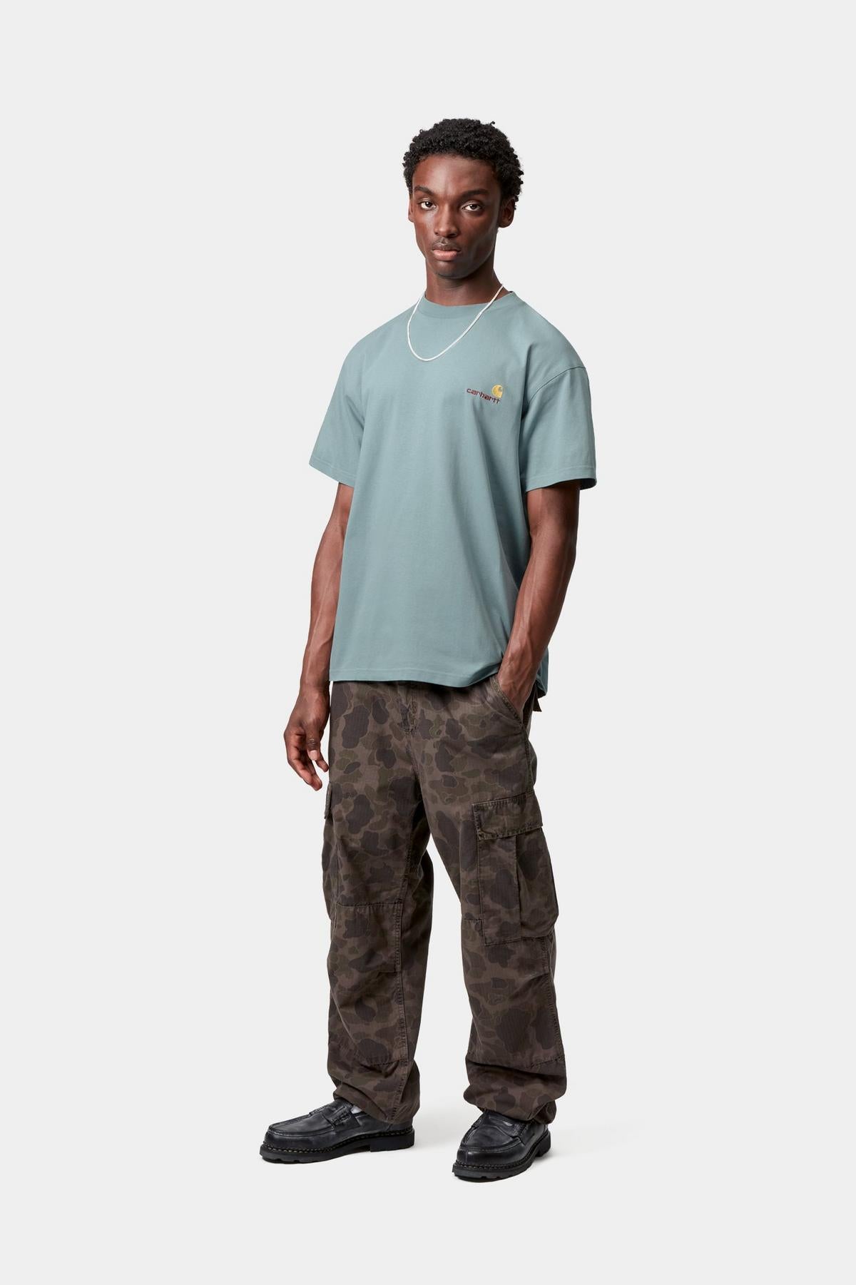 Man wearing a light blue t-shirt and camouflage pants on a white background