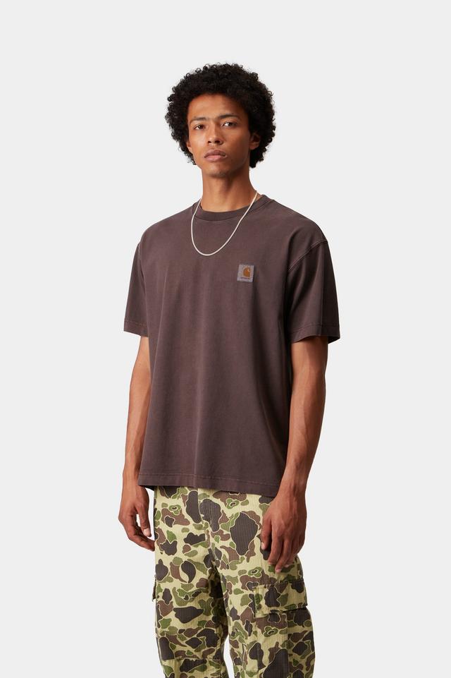 Man wearing a brown t-shirt with a logo and camouflage pants on a white background