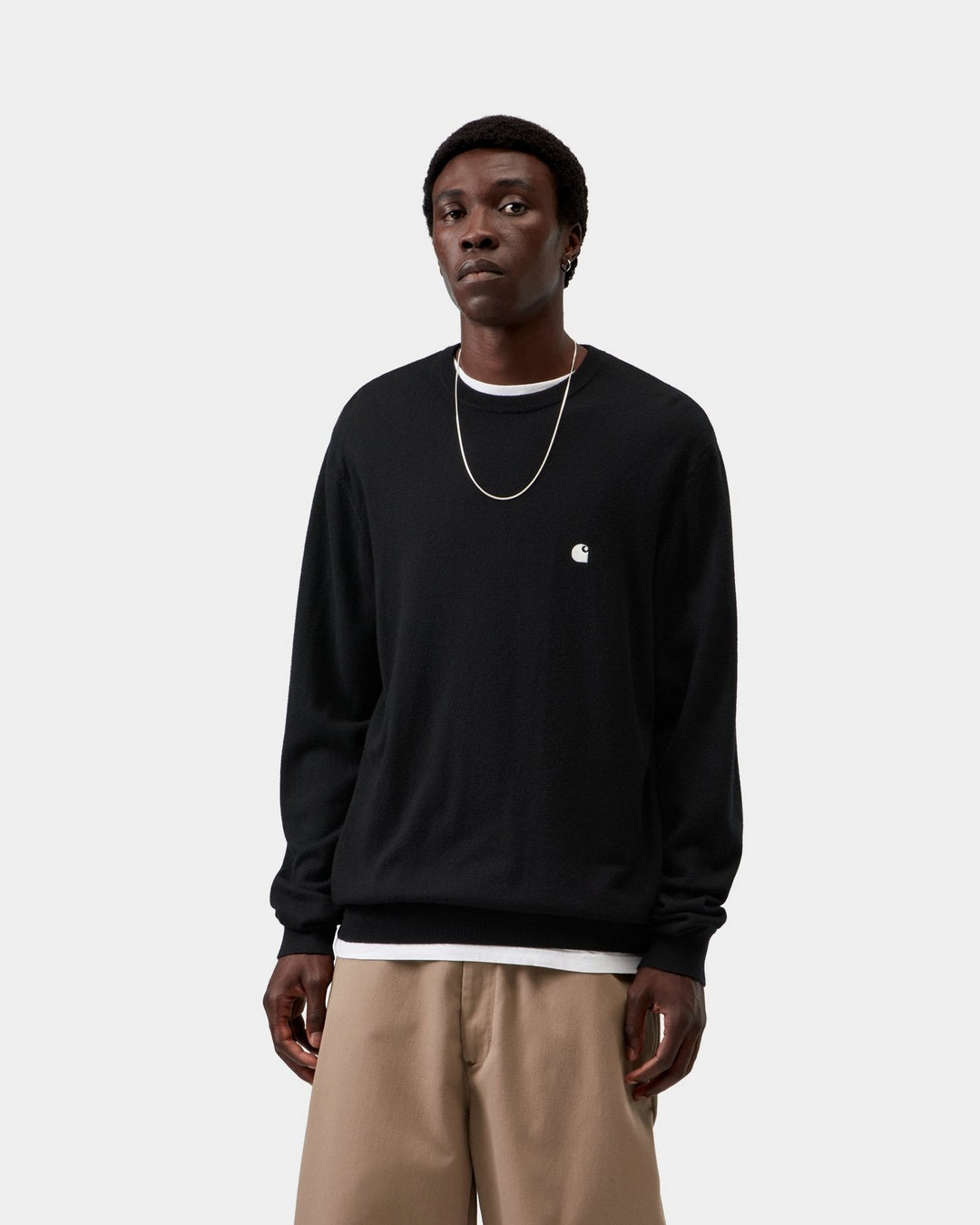 Carhartt WIP Madison Sweater in Black / Wax, front view, worn by model with small embroidered chest logo.