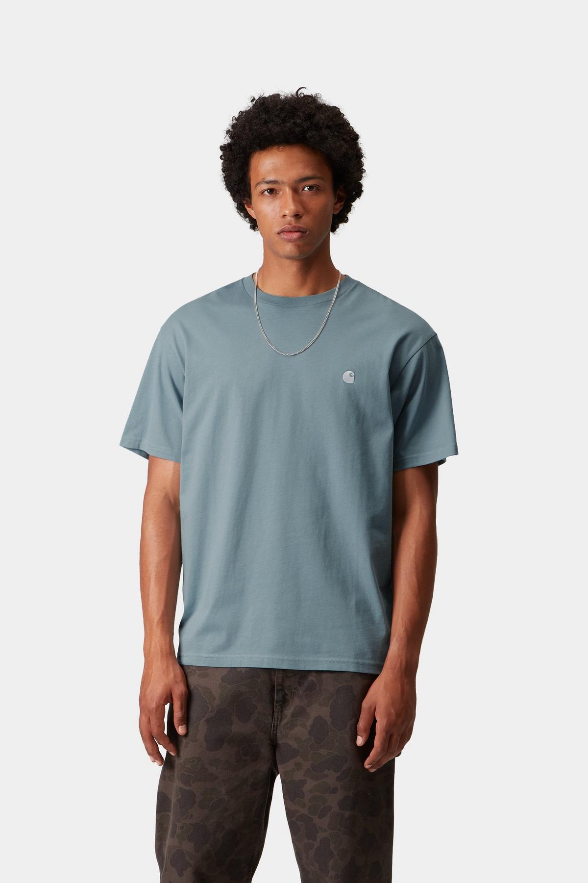 Man wearing a light blue t-shirt with a small logo on a white background