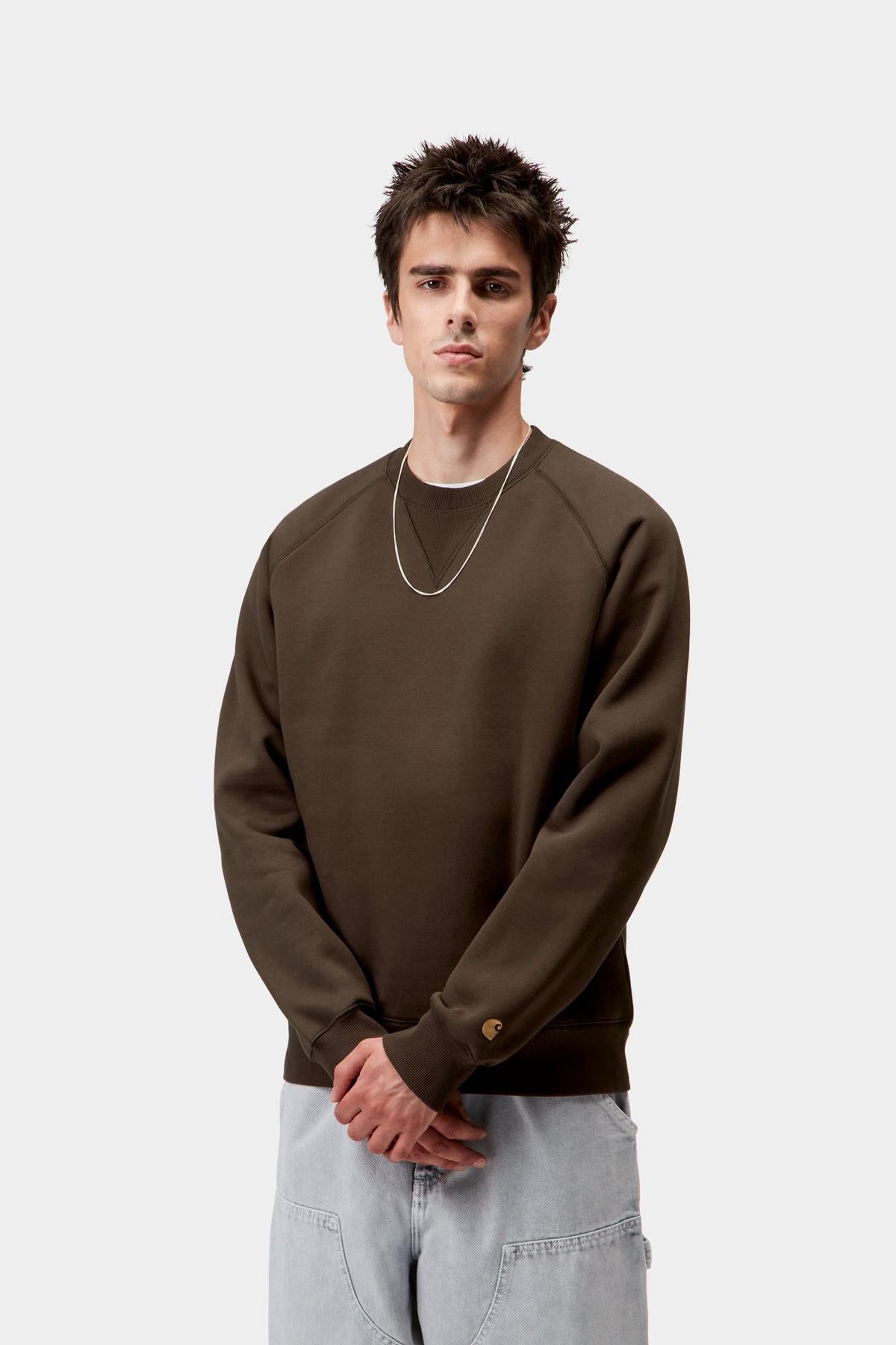 Man wearing a brown sweatshirt and light gray pants on a white background