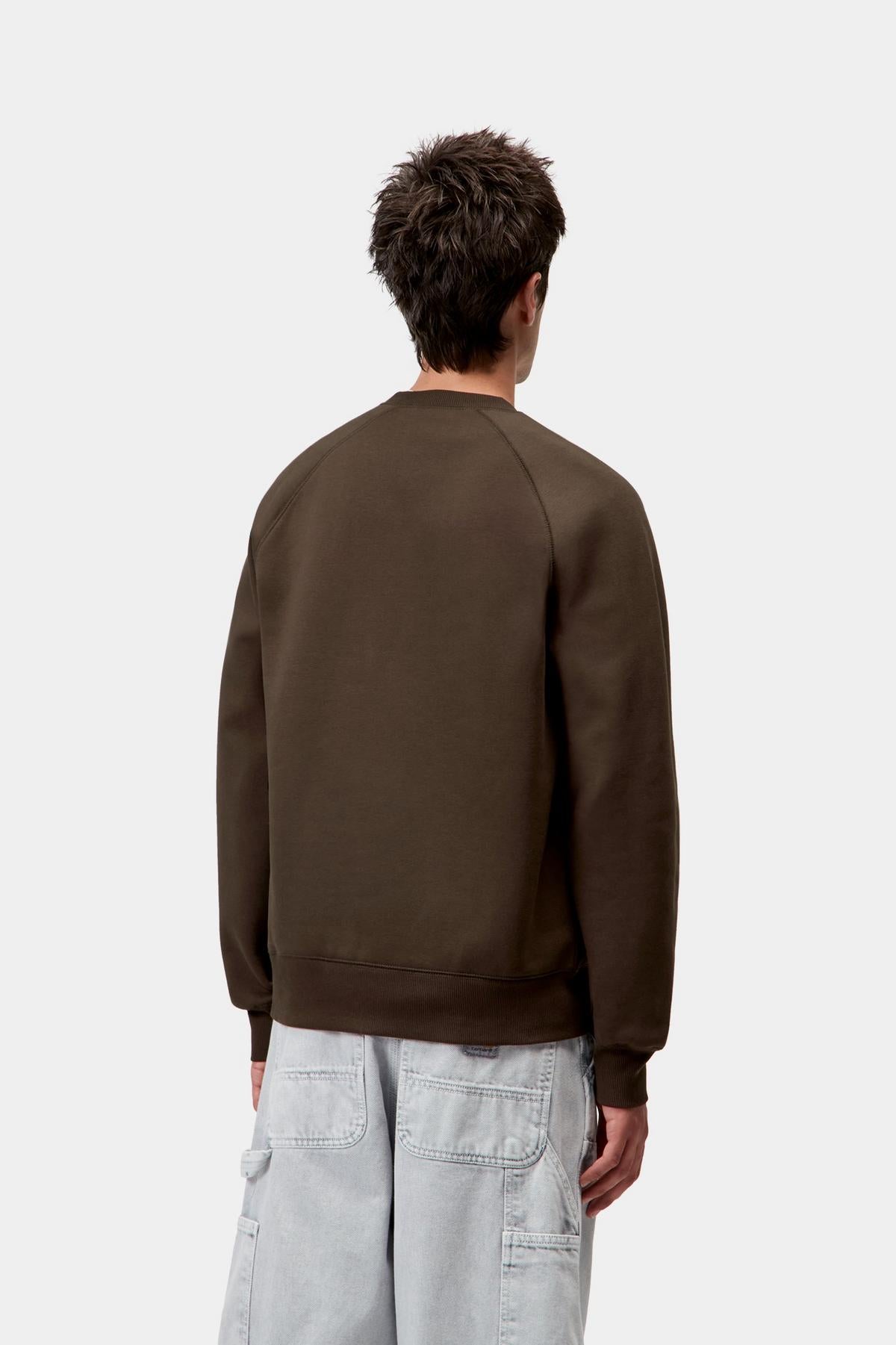 Person wearing a brown sweatshirt and light gray pants on a white background