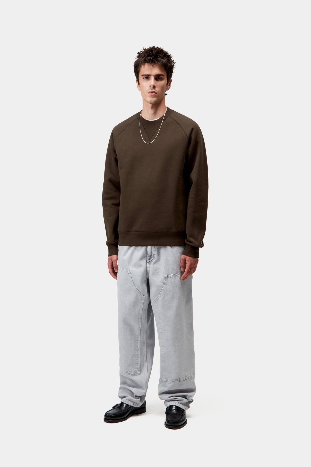 Person wearing a brown sweatshirt and gray pants on a white background
