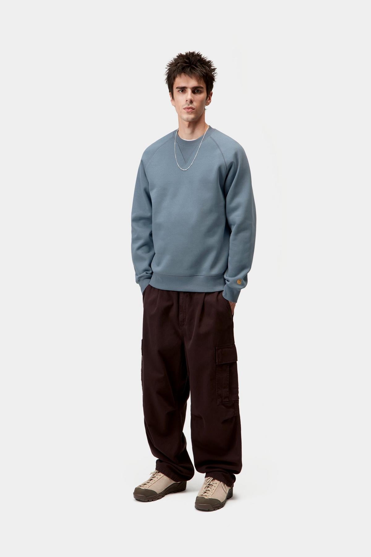 Man wearing a light blue sweater and dark brown pants on a white background