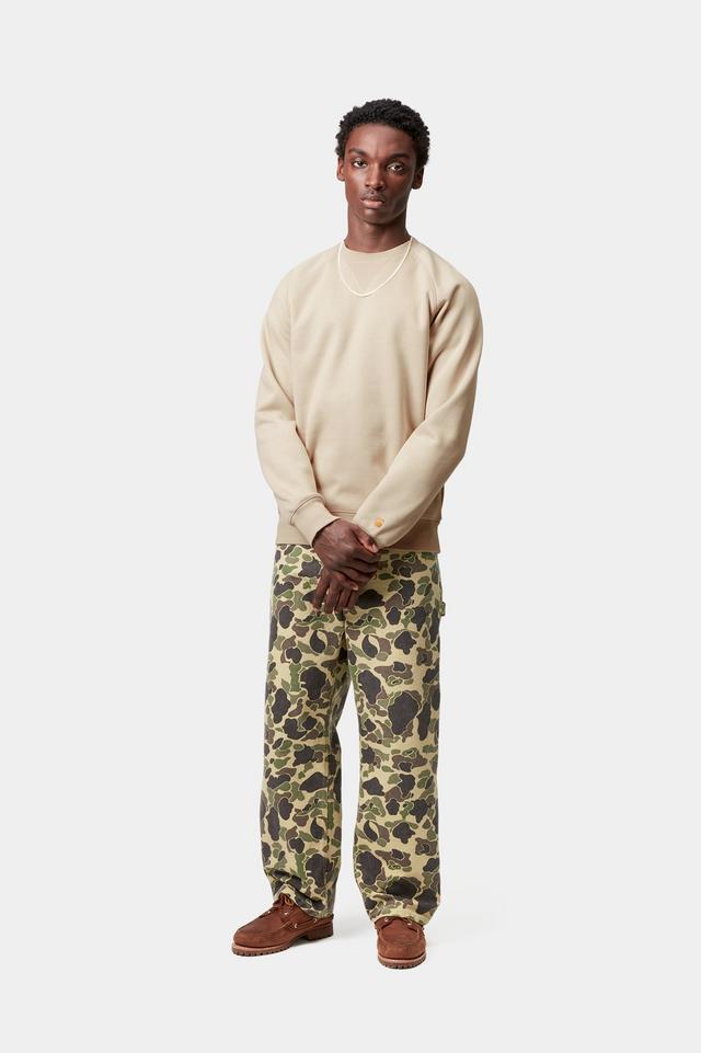 Man wearing a beige sweater and camouflage pants on a white background