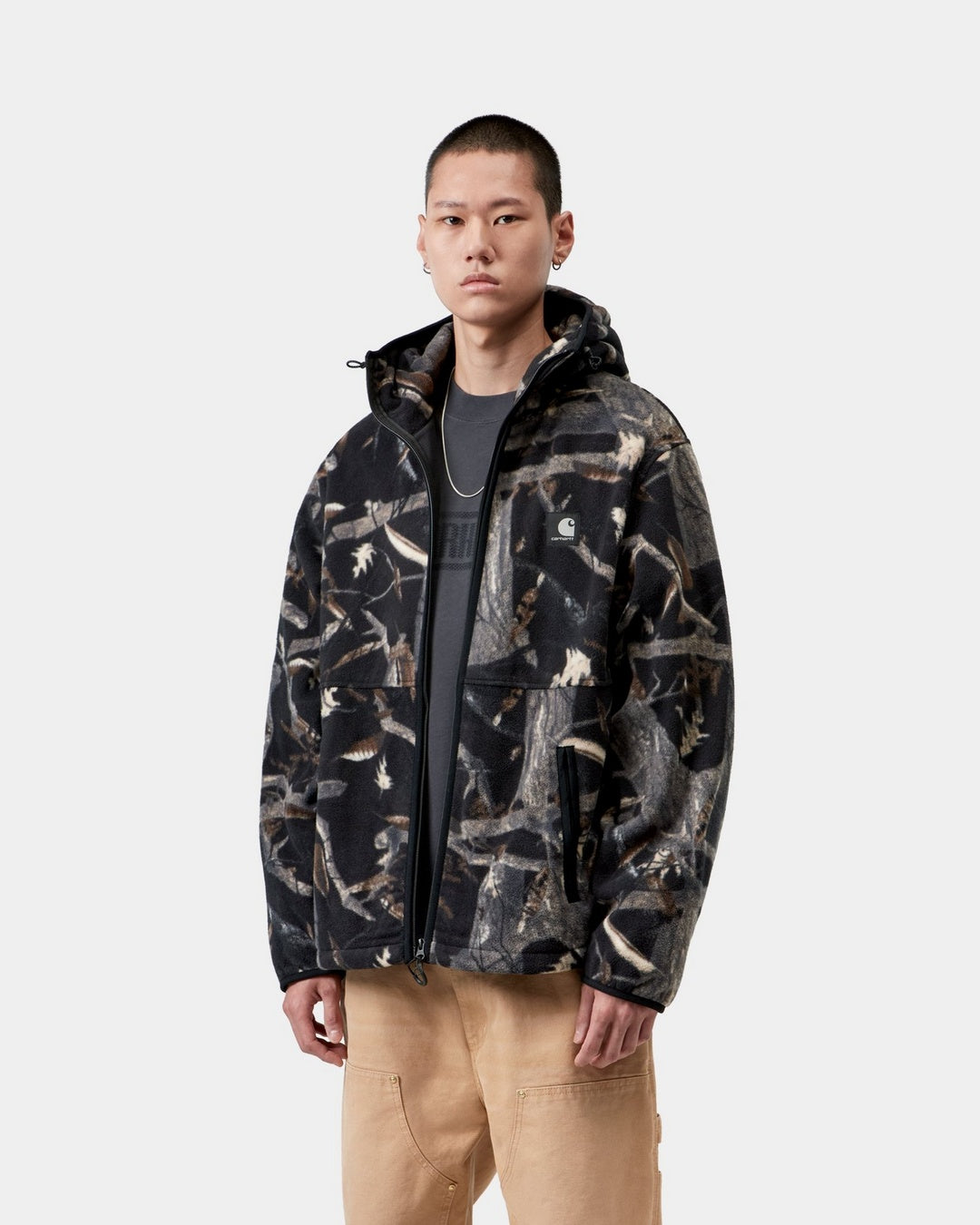 Carhartt WIP Blevin Liner in Camo Feather Tree, Black, shown worn front view with zip front, hood, and chest logo patch.