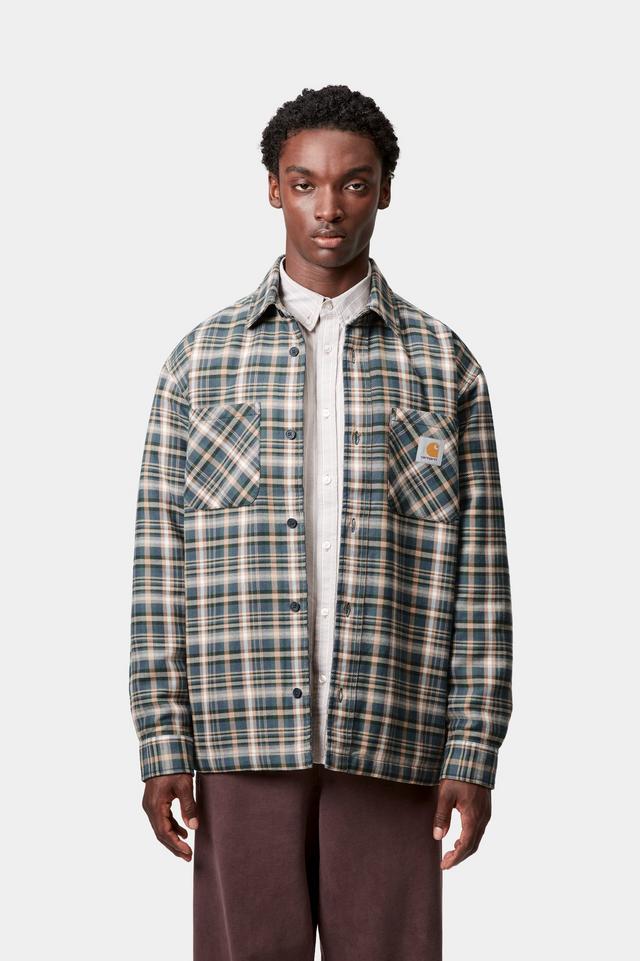 Man wearing a plaid shirt over a white collared shirt on a light gray background