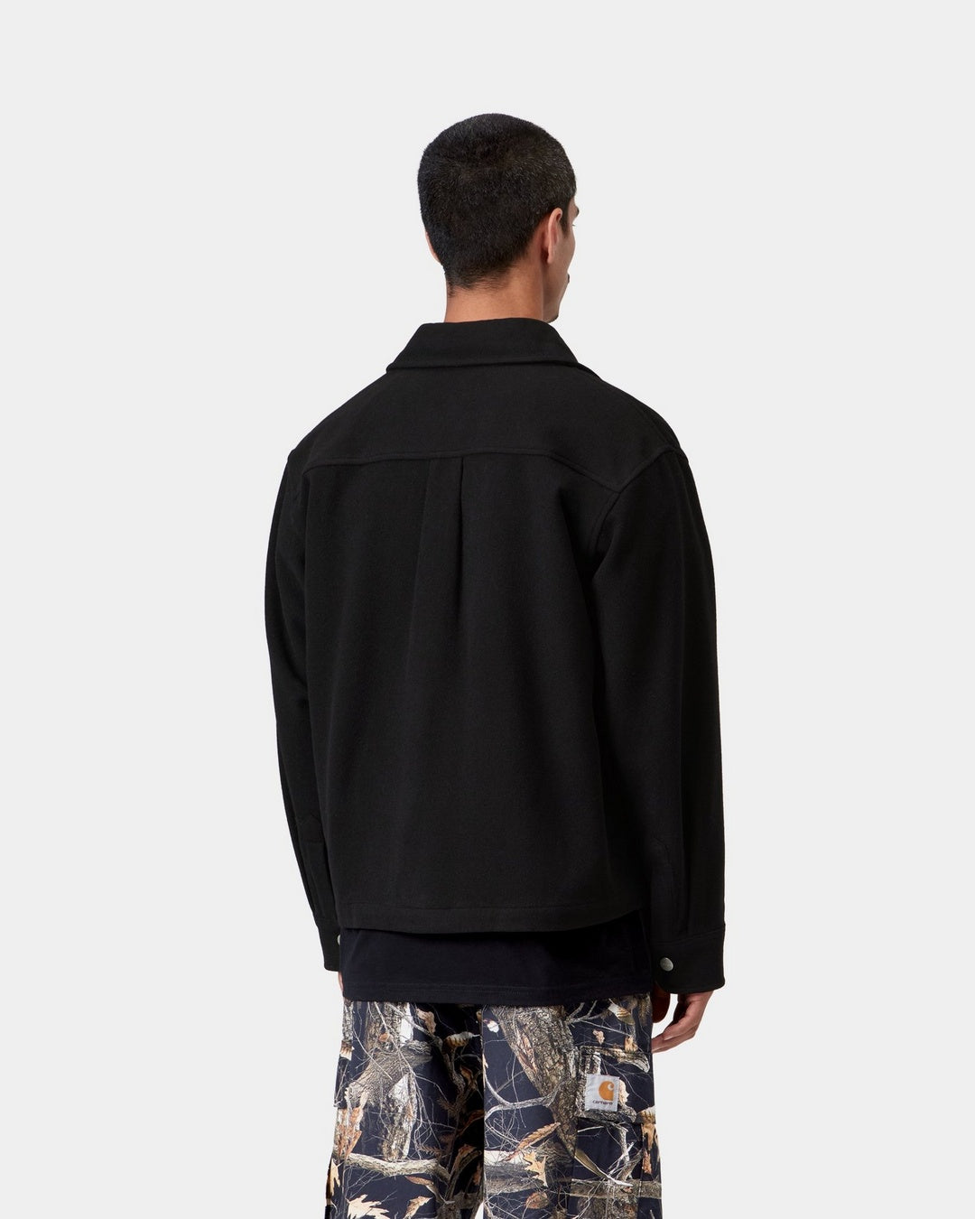 Back view of the Carhartt WIP Atoka Shirt Jac in Black, worn by a model. The unlined wool-blend jacket features a pointed collar, a back yoke with a centre box pleat, and a buttoned cuff on the sleeve.