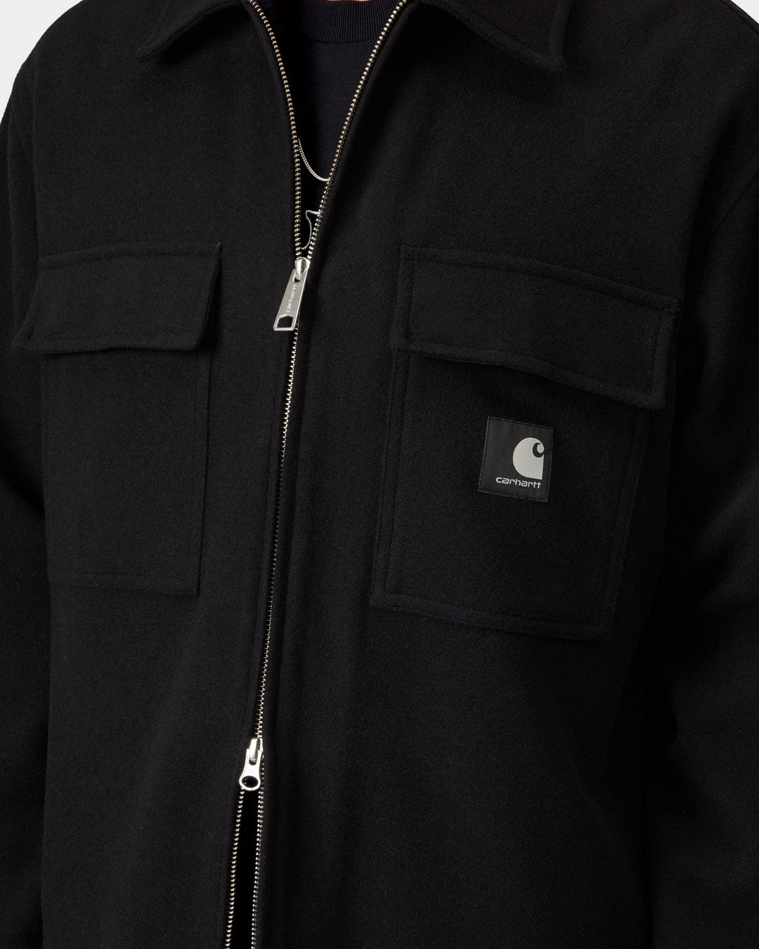 Close-up front view of the Carhartt WIP Atoka Shirt Jac in Black, showing the two-way silver zip closure, two chest flap pockets, and the black woven Square Label on the right pocket, shown on model.