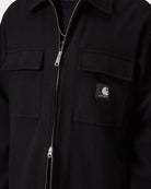 Close-up front view of the Carhartt WIP Atoka Shirt Jac in Black, showing the two-way silver zip closure, two chest flap pockets, and the black woven Square Label on the right pocket, shown on model.
