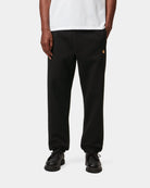 Carhartt WIP Chase Sweat Pant in Black / Gold, front view, with gold C logo on the leg.