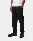Carhartt WIP Chase Sweat Pant in Black / Gold, shown on model with embroidered gold C logo on the front.