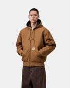 Carhartt WIP OG Active Jacket in WIP H Brown, front view on model with hood up and kangaroo pocket visible.