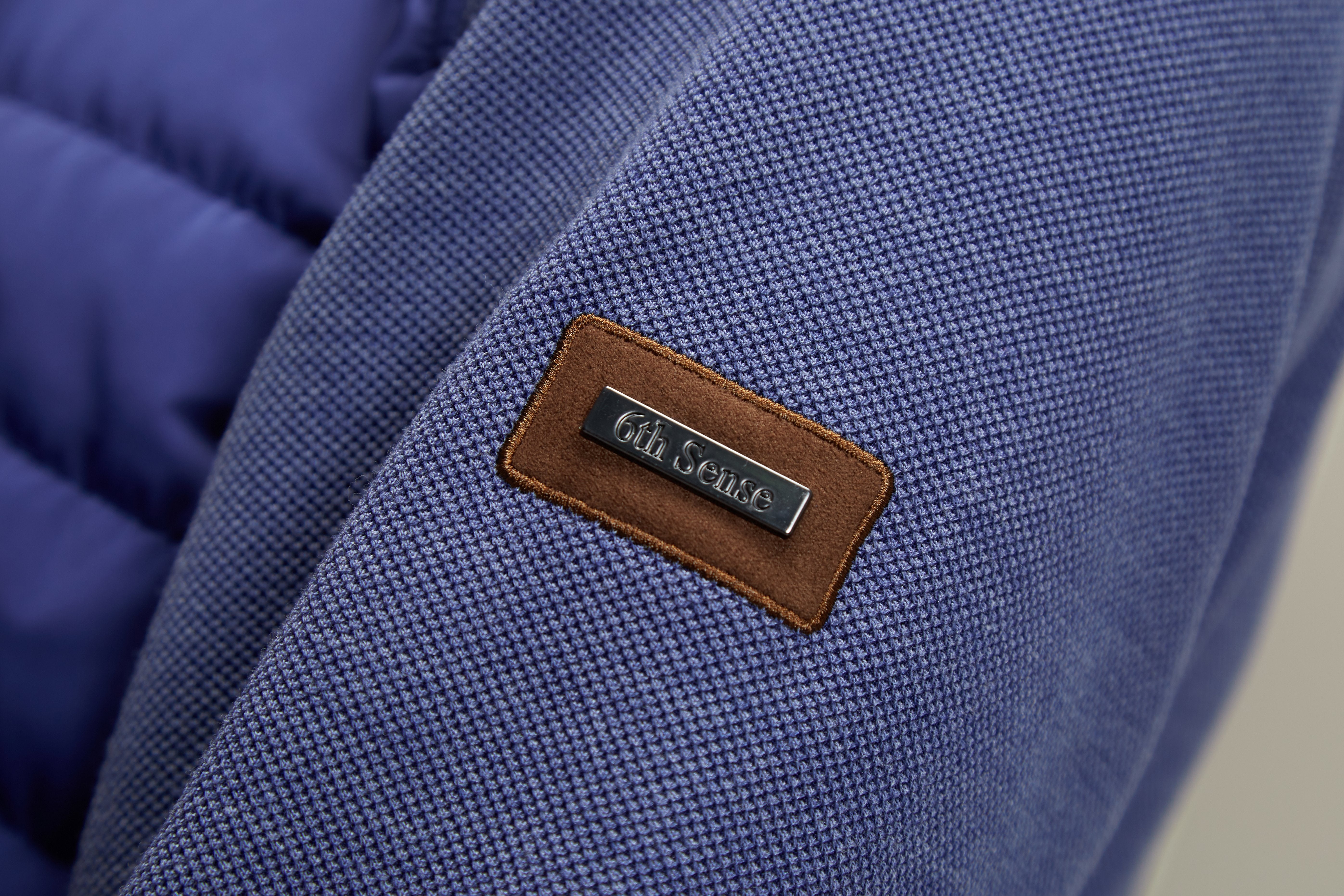 Close-up of a blue textured fabric with a brown leather label featuring '6th Sense' branding.