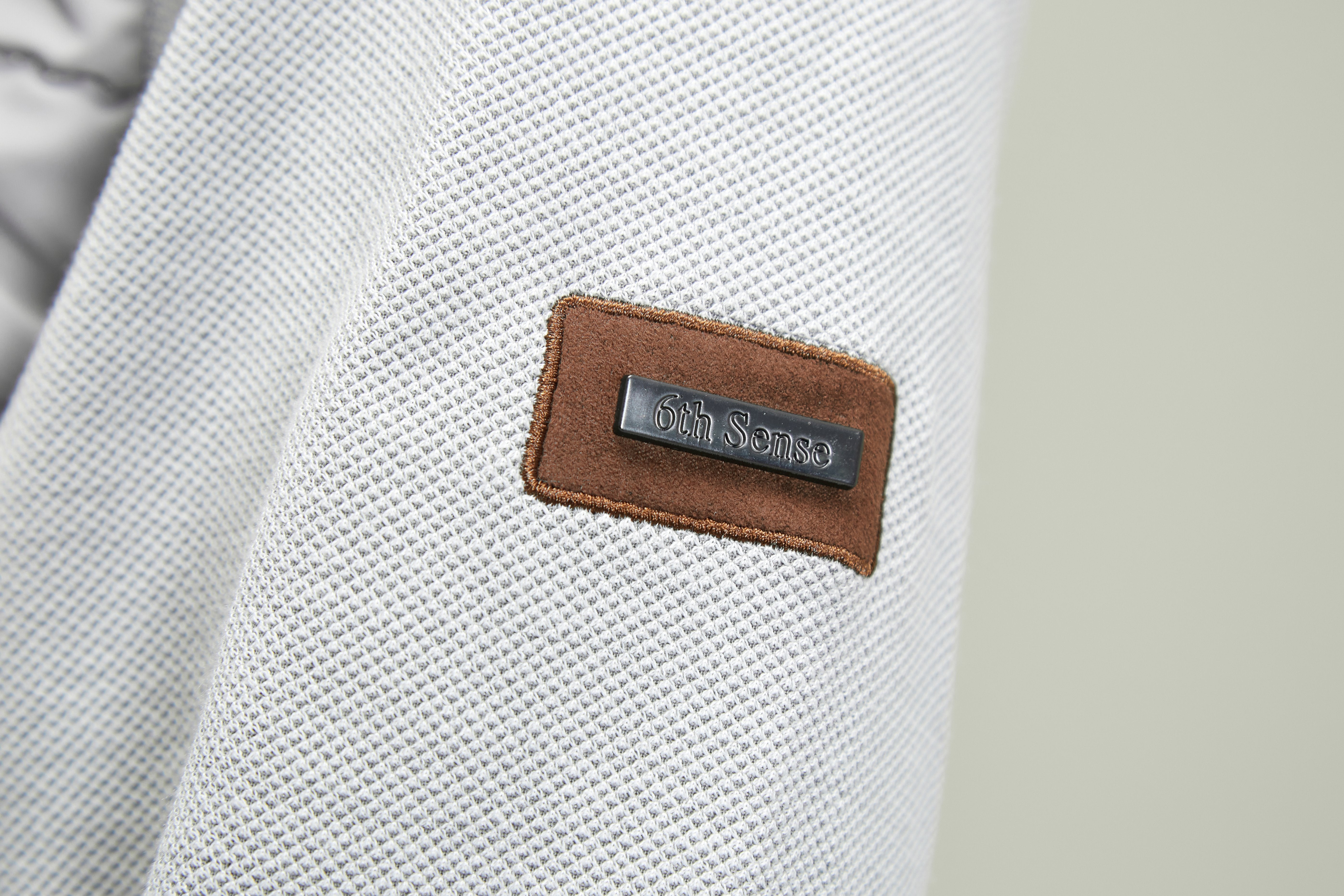 Close-up of a silver textured fabric with a brown label featuring '6th Sense' branding.