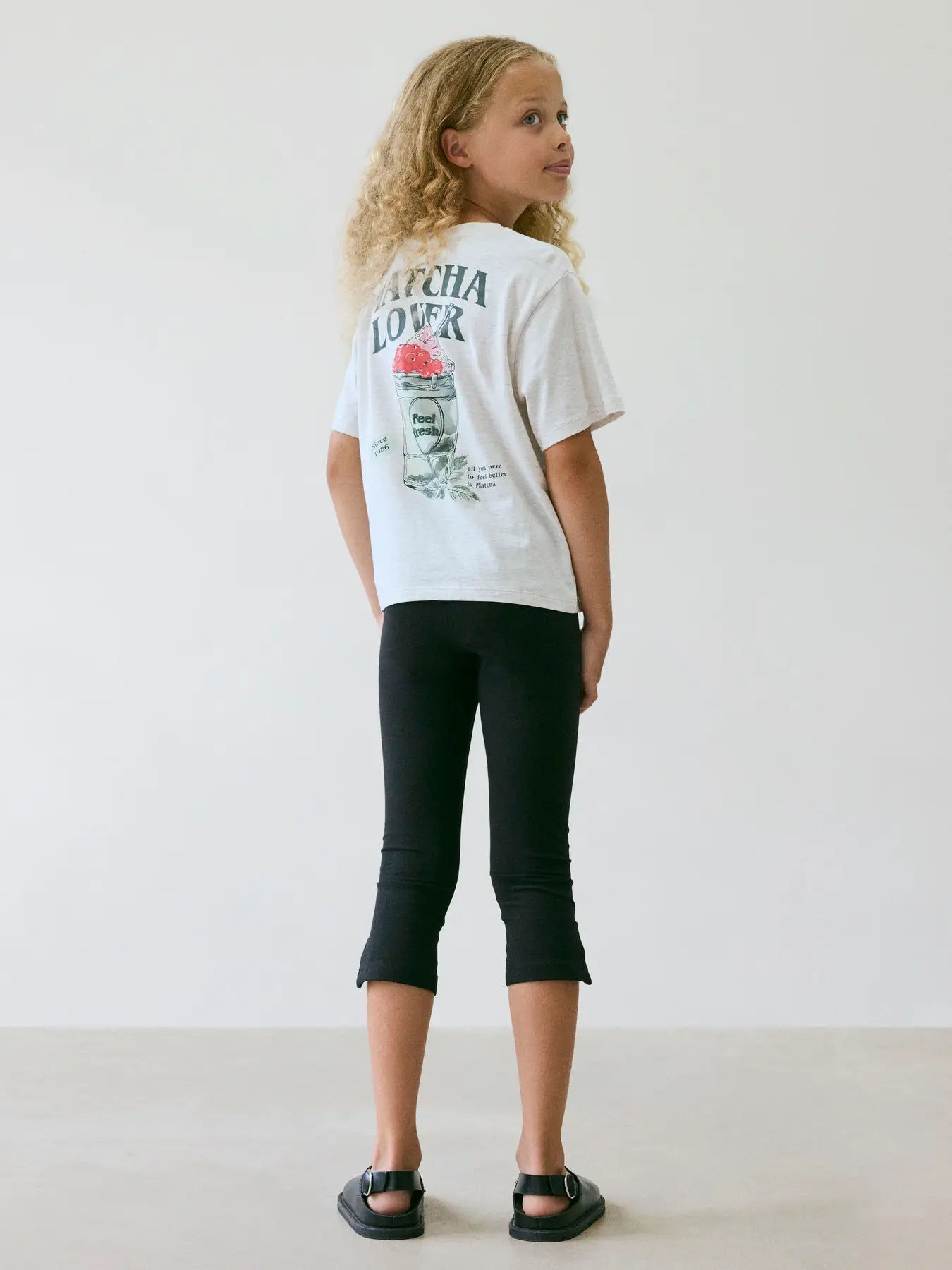 Child wearing a beige t-shirt with text and graphics, standing against a plain background
