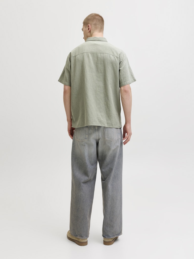 Person wearing montauk wavy texture short sleeve vetiver shirt and gray pants on a white background-Back view