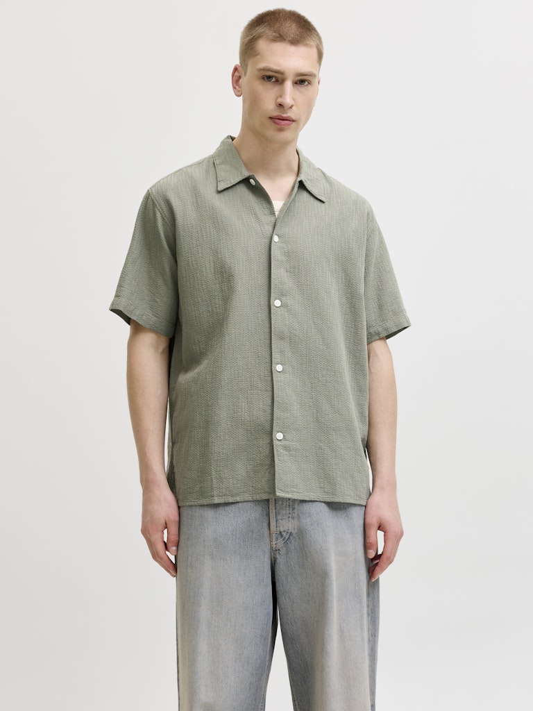 Man wearing a montauk wavy texture short sleeve verviter shirt and light gray pants on a white background