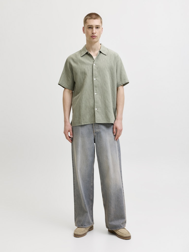 Man wearing montauk wavy texture short sleeve vetiver shirt and gray pants on a white background