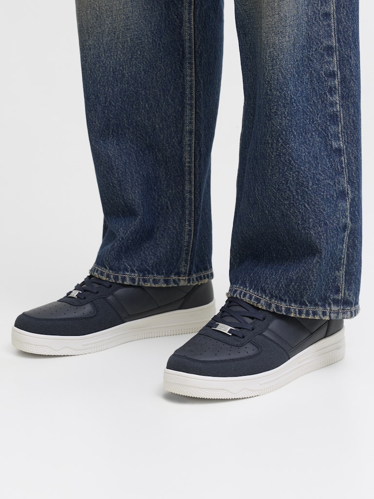 Navy sneakers worn with blue jeans on a white background
