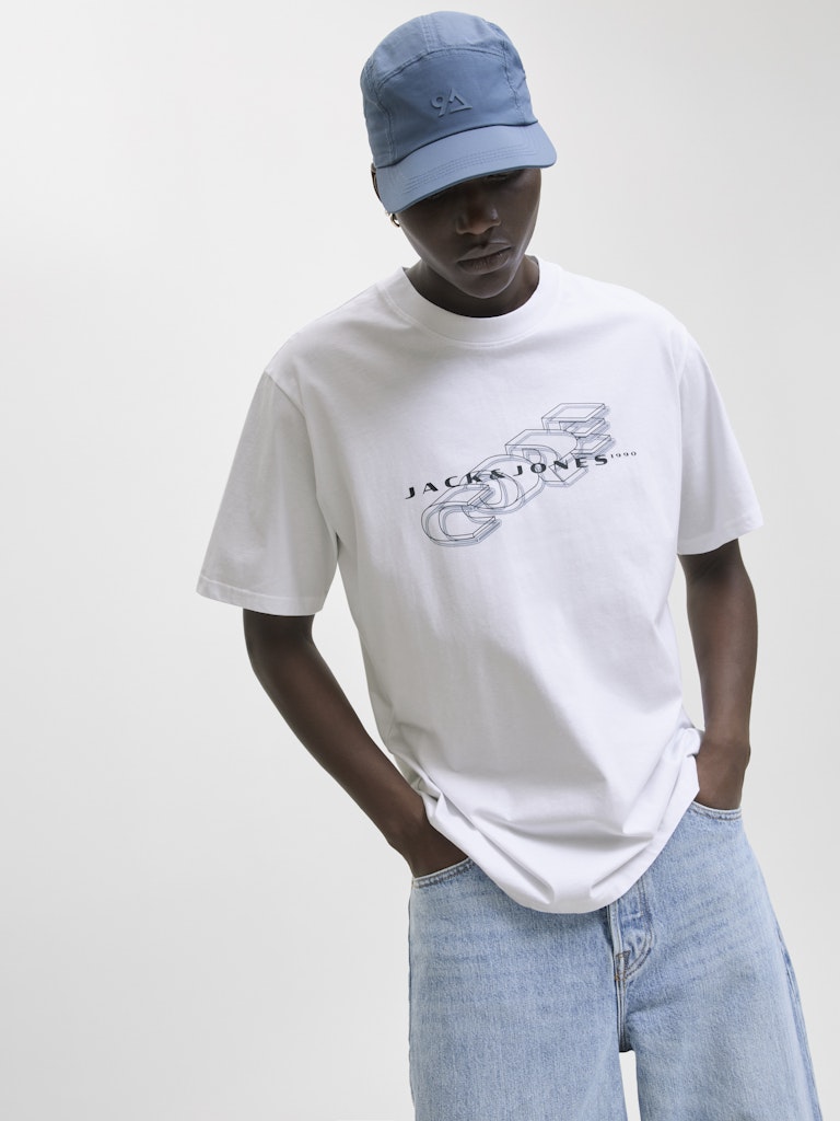 Person wearing a white t-shirt with a graphic design and a blue cap on a plain background
