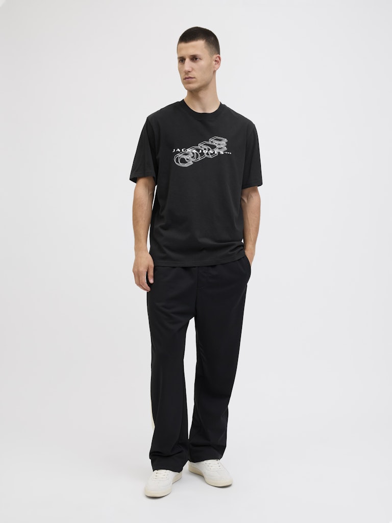 Man wearing a black t-shirt with a logo and black pants on a white background